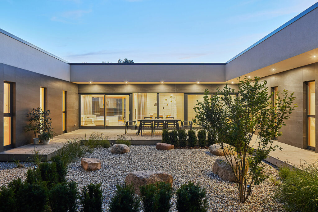 Evening courtyard of Villa AJ with landscaped stone garden, outdoor dining area, recessed lighting and full-height glazing connecting interior living spaces, designed by NG Architects