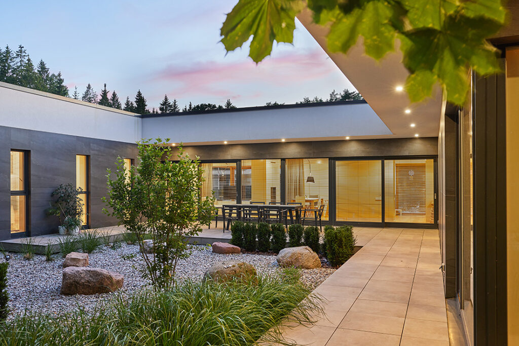 Evening courtyard of Villa AJ with landscaped garden, outdoor dining area, recessed lighting and full-height glazing connecting interior spaces, designed by NG Architects