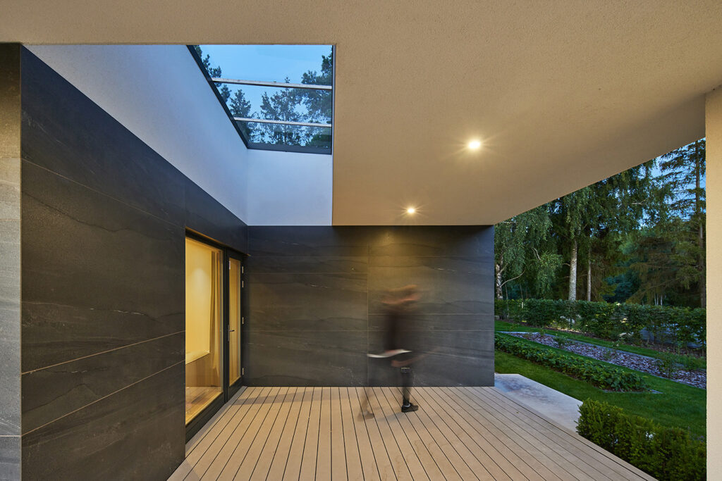 Covered terrace of Villa AJ with skylight opening, dark cladding panels, wooden decking, and evening atmosphere, designed by NG Architects