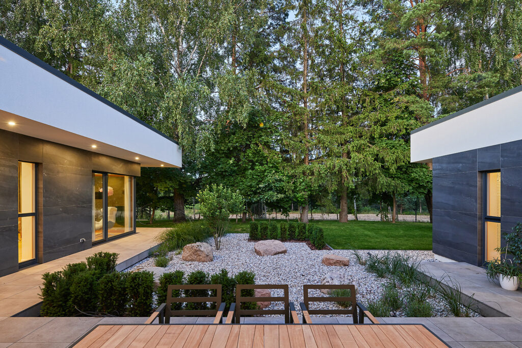 Courtyard garden of Villa AJ with stone landscaping, greenery, recessed façade lighting and open connection to surrounding forest, designed by NG Architects