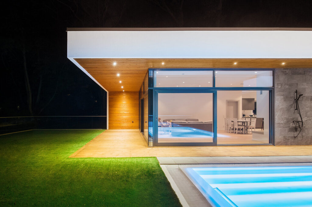 Modern Scandinavian villa with illuminated pool and glass façade opening to terrace at night